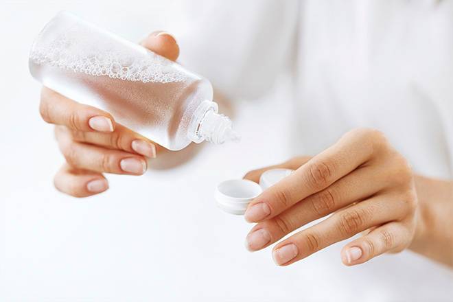 Mãos de mulher a aplicar líquido para lentes de contacto